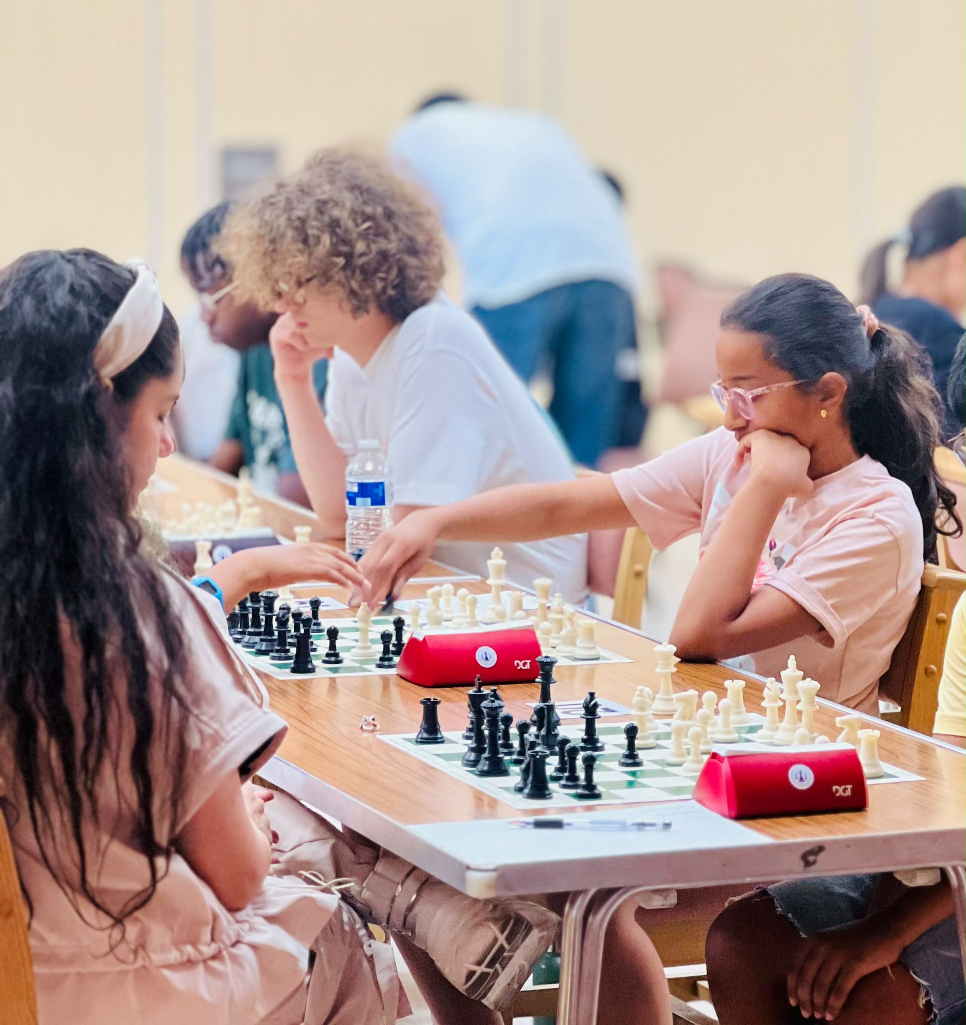 Two junior girls focused on their chess games at a tournament, chess clocks on the table