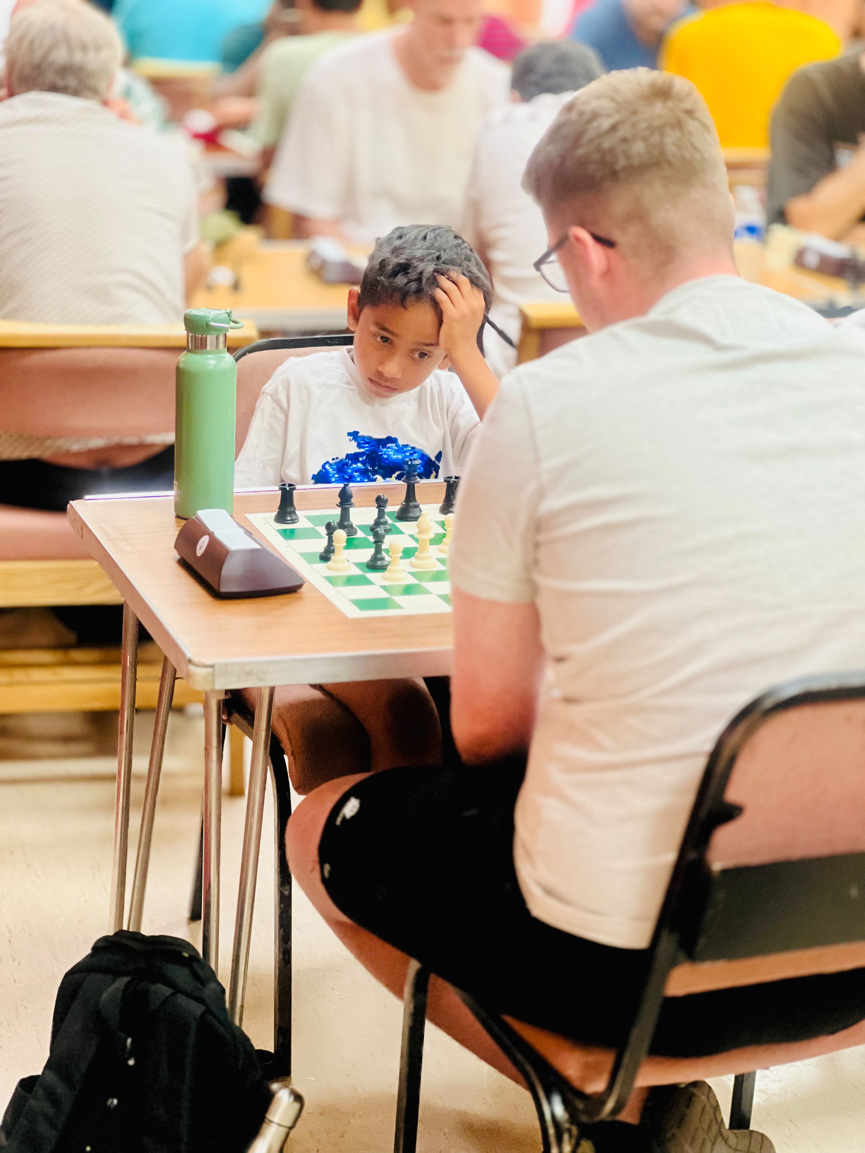 Young boy with hand on head thinking carefully about his next move against an adult opponent