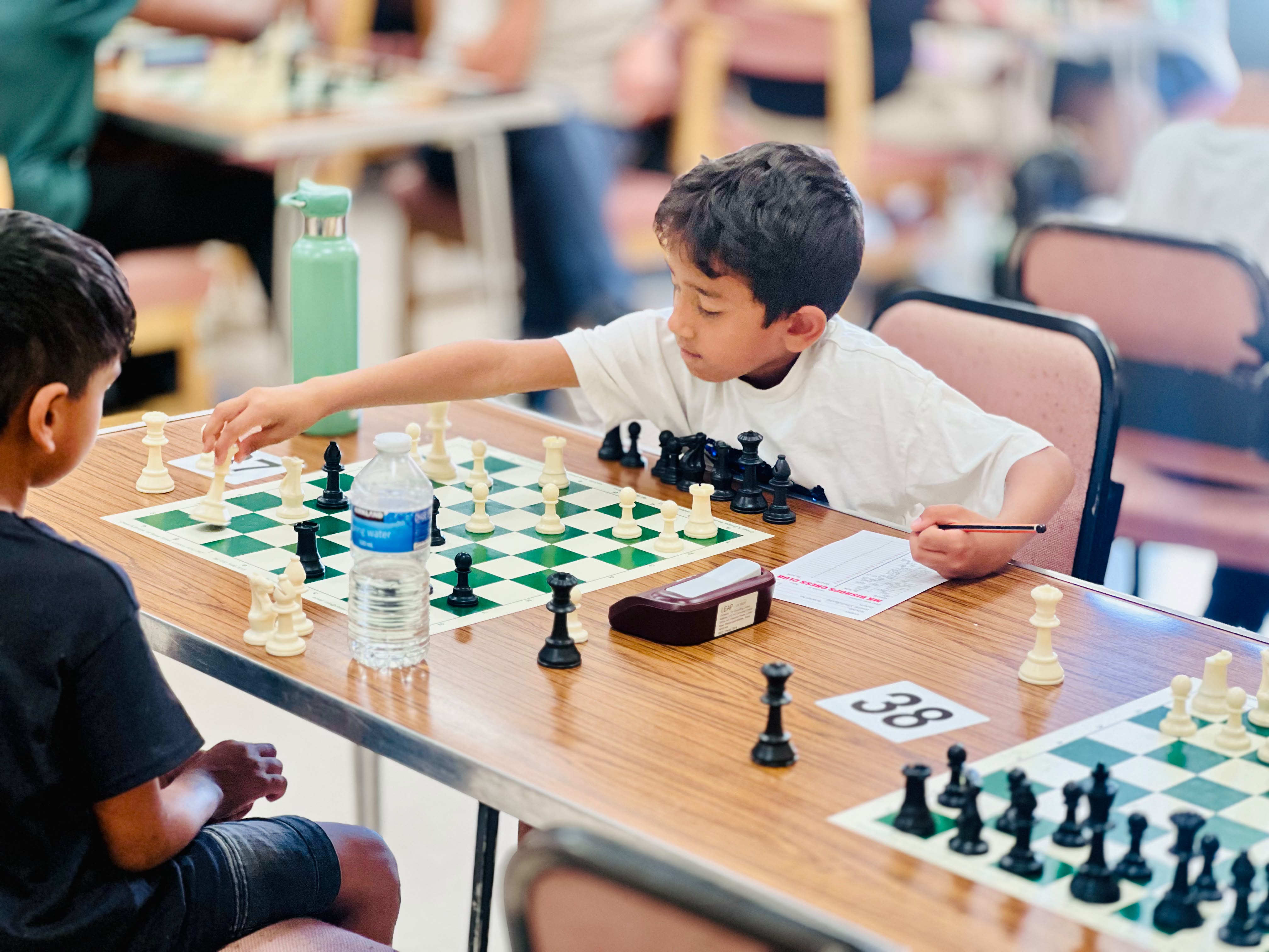 Young junior player reaching to make his move on board 38 in a tournament hall full of competitors